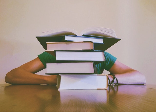 College Books Piled Over a Student's Head